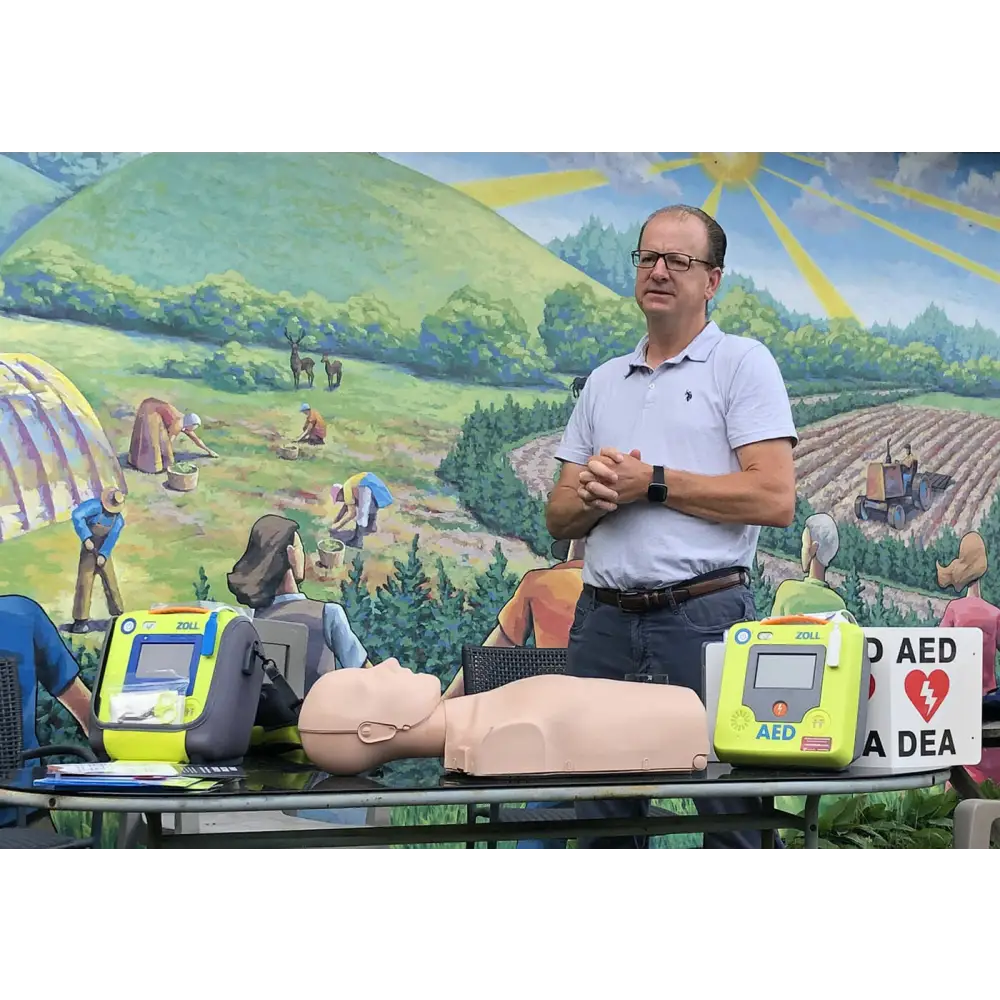 A man standing behind a CPR training doll, AEDs and various accessories