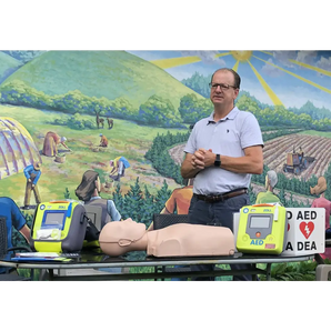 A man standing behind a CPR training doll, AEDs and various accessories