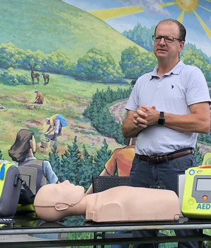 A man standing behind a CPR training doll, AEDs and various accessories